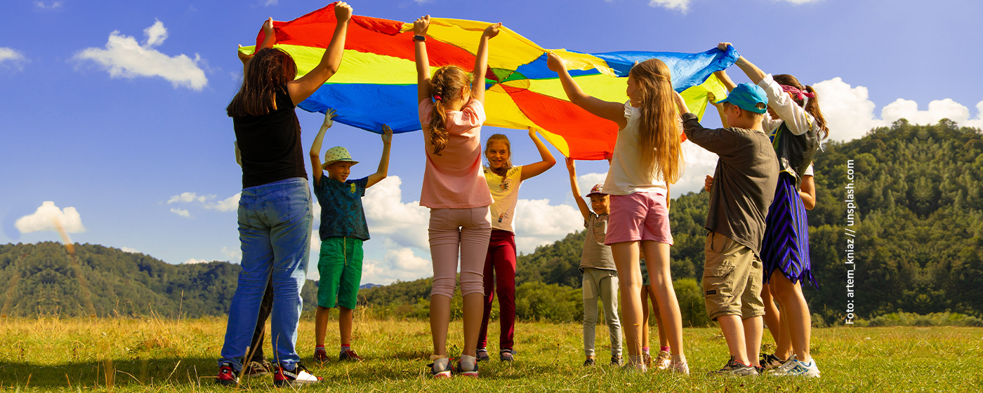 Spiel bei Ferienfreizeit: Kinder halten ein bunten Tuch in die Luft