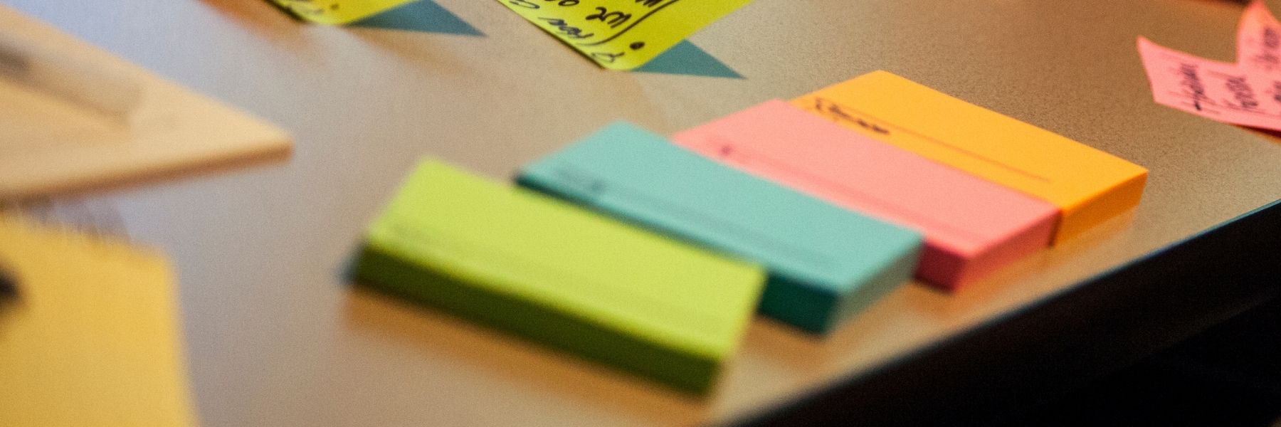 Auf einem Tisch liegen vier Stapel bunte Post-It's, dahinter kleben schon sehr viele beschriftete Klebezettel auf dem Tisch.