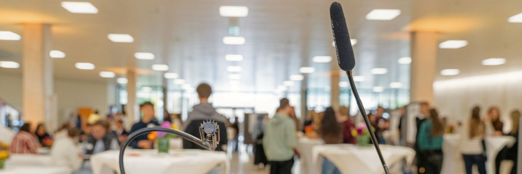 Im Vordergrund ist ein Mikrofon zu sehen, im Hintergrund das Foyer des Landtags von Baden-Württemberg, das voll mit jungen Menschen ist.