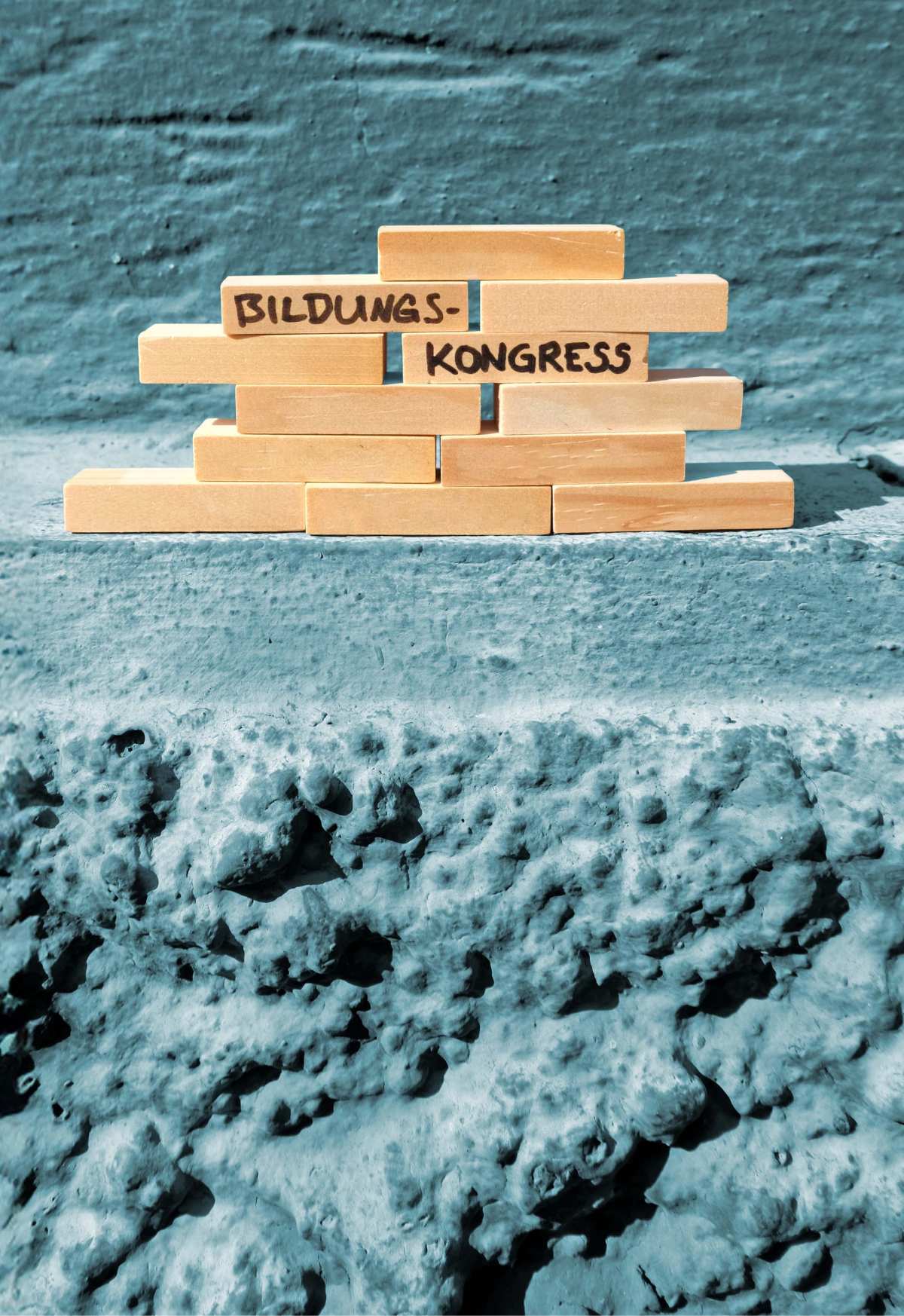 Eine blaue Mauer, auf denen mehrere Holzbausteine zu einem kleinen Turm gebaut sind. Auf ihnen steht "Bildungskongress".
