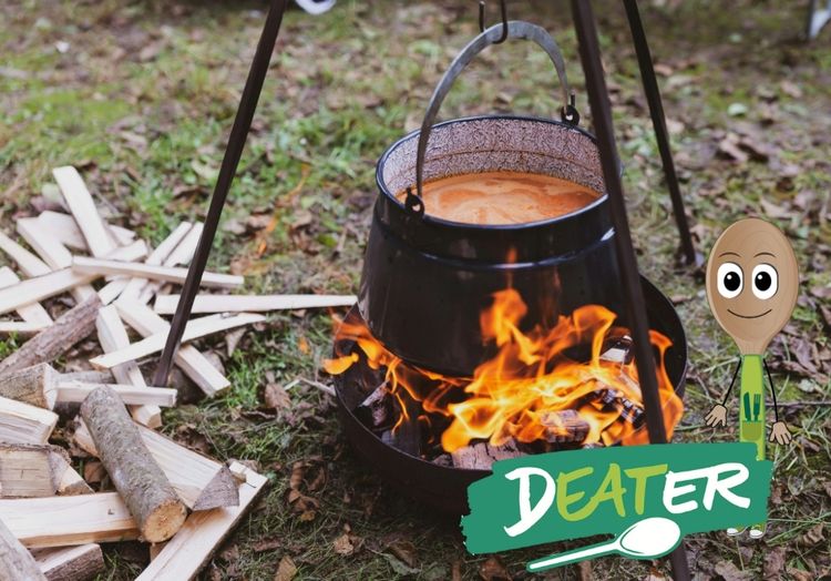 In einem großen Kessel über einem Lagerfeuer köchelt eine Suppe.