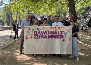 Ein Gruppenbild von Personen, die im unter einem großen Baum stehen und einen Banner "BAWÜ hält zusammen" hochhalten. Einer der abgebildeten Personen ist MP Özdemir.