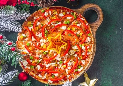 Festtagsstimmung: die Viertel einer Pizza sind so übereinander gelegt, dass sie einen Weihnachtsbaum ergeben. Drumherum liegt weihnachtliche Deko.