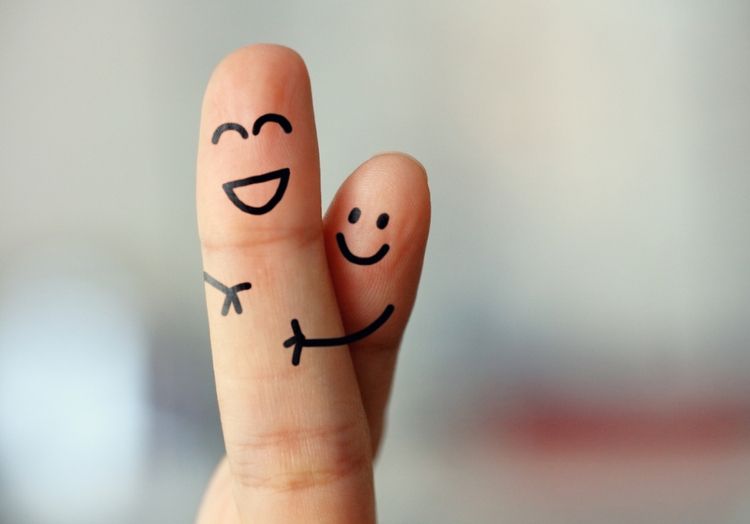 Auf zwei Fingern sind zwei lachende Gesichter aufgemalt. Die Finger werden so gehalten, dass es aussieht als würde ein Finger den anderen umarmen.